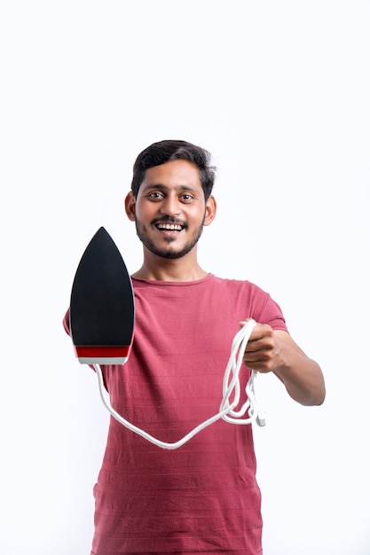 Sorrindo dono de casa jovem atraente no avental segurar nas mãos de ferro enquanto fazia o trabalho doméstico isolado no retrato de estúdio de fundo amarelo. Conceito de limpeza.