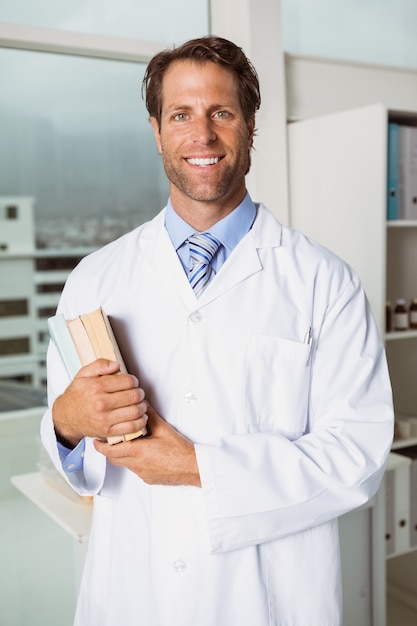 Sorrindo, doutor masculino, segurando, livros, em, escritório médico