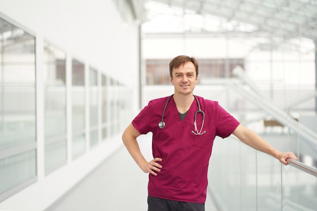Sorrindo doutor masculino weared em Borgonha roupa nos corredores brancos da clínica