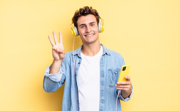 Sorrindo e parecendo amigável, mostrando o número três ou terceiro com a mão para a frente, em contagem regressiva. conceito de fones de ouvido e smartphone