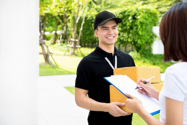 Sorrindo entregador de uniforme preto, entregando caixas de encomendas para uma mulher