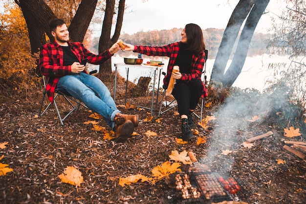 Sorrindo feliz casal descansando perto do fogo cozinhando comida