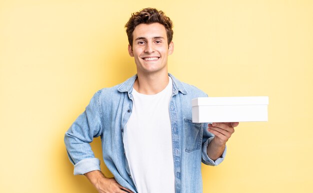 Foto sorrindo feliz com uma mão no quadril e atitude confiante, positiva, orgulhosa e amigável. conceito de caixa branca