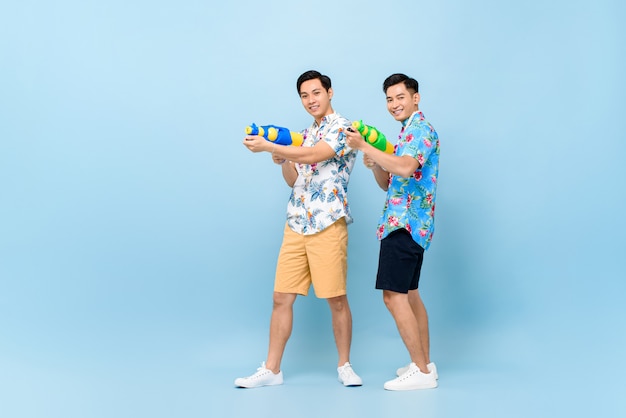 Sorrindo felizes amigos do sexo masculino brincando com pistolas de água para o festival songkran na tailândia e sudeste da ásia