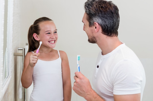 Sorrindo, filha e pai segurando uma escova de dentes no banheiro