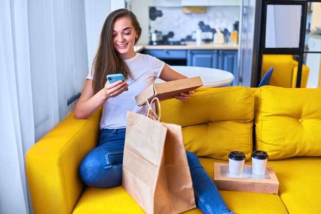 Foto sorrindo fofo satisfeito feliz adulto casual alegre jovem milenar comprador recebeu sacos de papelão com comida para viagem e bebidas em casa. conceito de serviço de entrega rápida