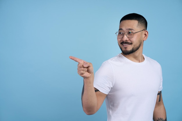 Sorrindo homem barbudo asiático apontando para o espaço de cópia lateral com uma mão