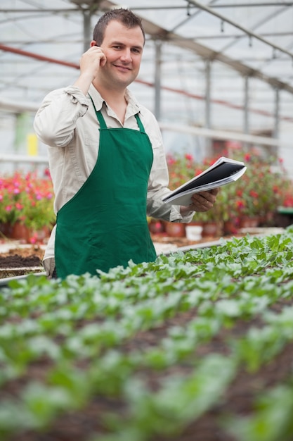 Sorrindo homem no telefone e tomando notas em casa de vegetação