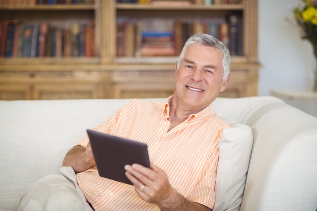 Sorrindo homem sênior usando tablet digital na sala de estar