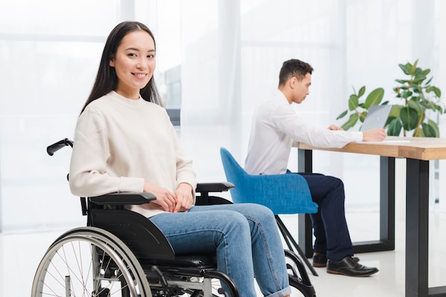 Foto sorrindo, incapacitado, mulher jovem, sentando, ligado, cadeira rodas, olhando câmera, frente, homem, trabalhar, laptop