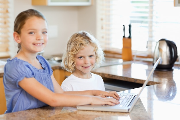 Sorrindo irmãos no laptop na cozinha