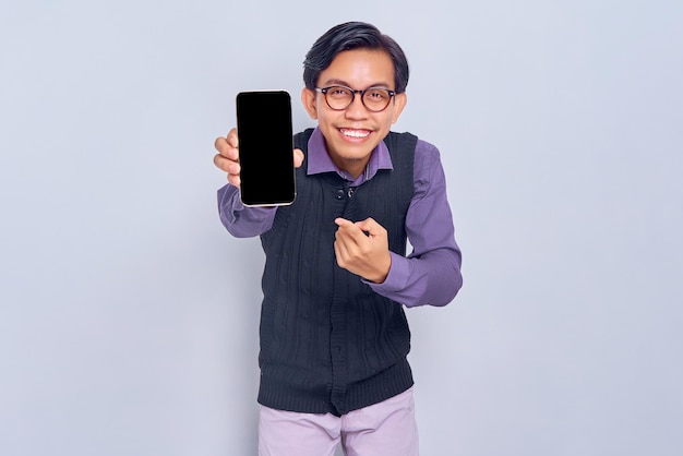 Sorrindo jovem asiático em camisa casual e colete mostrando celular de tela em branco recomendando aplicativo móvel isolado em fundo branco Conceito de estilo de vida de pessoas