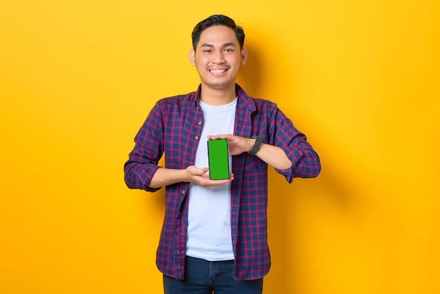 Sorrindo jovem asiático em camisa xadrez mostrando smartphone de tela em branco isolado em fundo amarelo