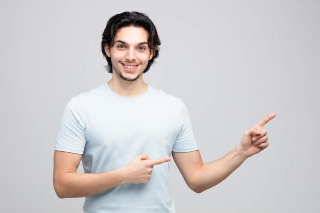 sorrindo jovem bonito olhando para a câmera apontando para o lado isolado no fundo branco