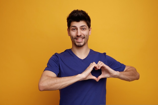 Sorrindo jovem bonito olhando para a câmera fazendo gesto de amor em fundo amarelo