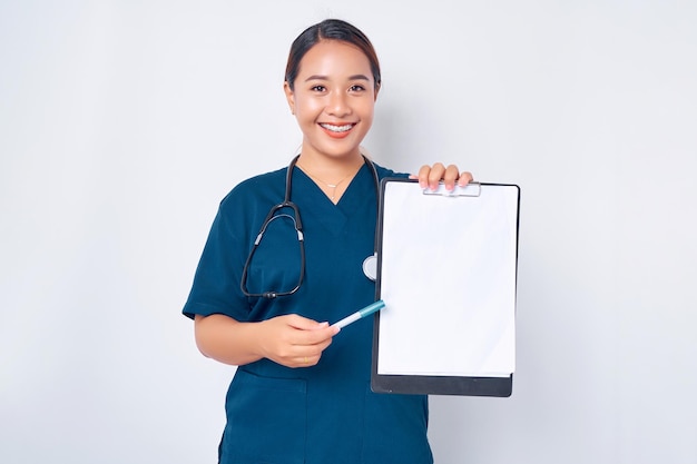Sorrindo jovem enfermeira asiática vestindo uniforme azul com um estetoscópio segurando prancheta e caneta explica informações na prancheta apontando papel no fundo branco Conceito de medicina de saúde