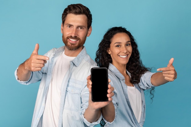 Sorrindo jovem europeu e mulher árabe mostram dedos no smartphone com tela em branco