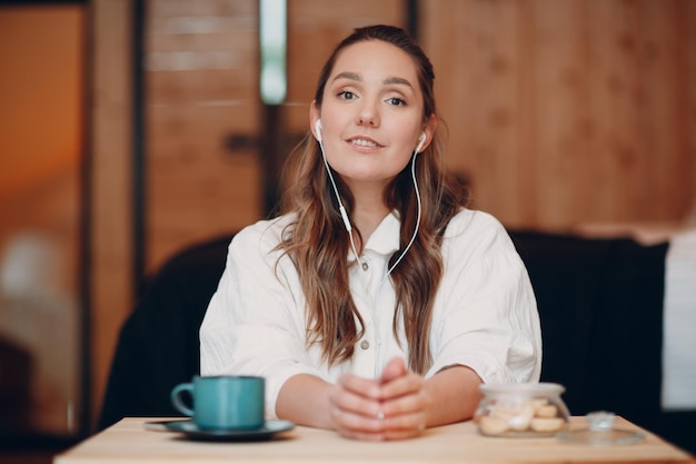 Sorrindo jovem feliz sentada à mesa em casa atrás do laptop do computador e falando em videochamada menina feminina com fones de ouvido móveis portáteis falando on-line na webcam dentro de casa