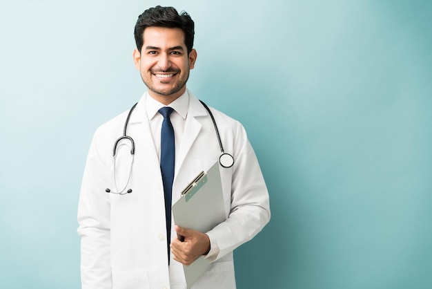 Sorrindo jovem médico masculino segurando a prancheta em pé contra um fundo colorido