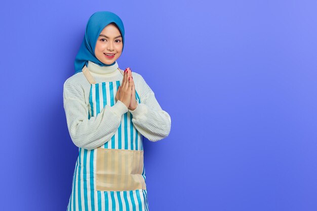 Sorrindo jovem muçulmana asiática em 20 anos usando hijab e avental sinal aberto para cumprimentar e cumprimentar os clientes isolados no fundo roxo Pessoas dona de casa conceito de estilo de vida muçulmano