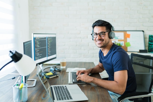 Sorrindo jovem programador freelance masculino latino sentado com tecnologia na mesa