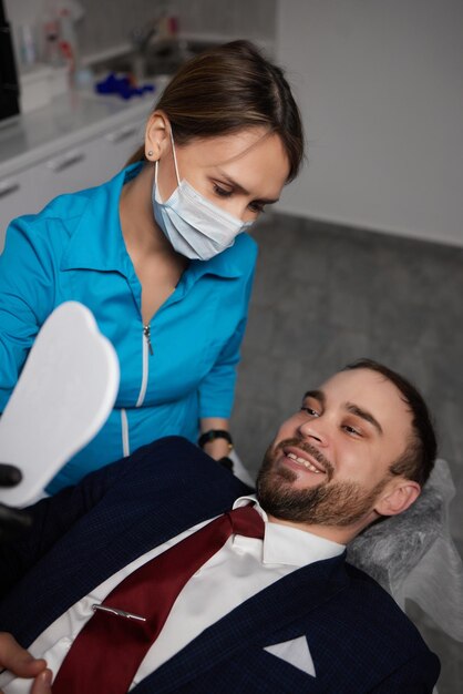 Foto sorrindo jovem sentado na cadeira do dentista enquanto médico examinando seus dentes