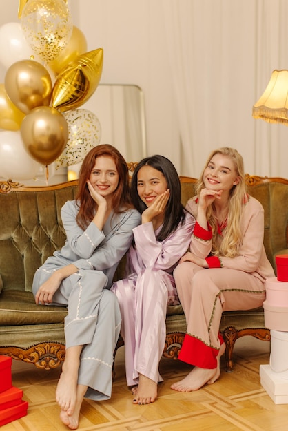 Sorrindo jovens modelos interraciais de pijama fazem foto juntos enquanto passam o tempo na festa do pijama roupas confortáveis para dormir conceito de descanso em casa