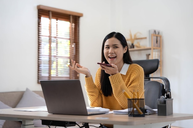 Sorrindo linda empresária asiática analisando gráfico e gráfico mostrando mudanças no mercado e segurando smartphone em casa