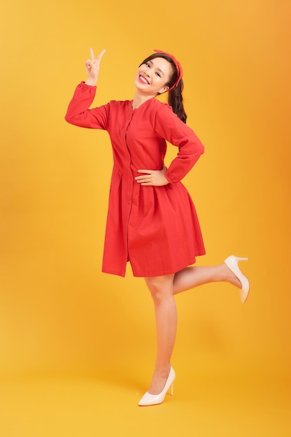 Sorrindo linda jovem de vestido vermelho elegante está segurando as mãos no quadril e olhando para longe