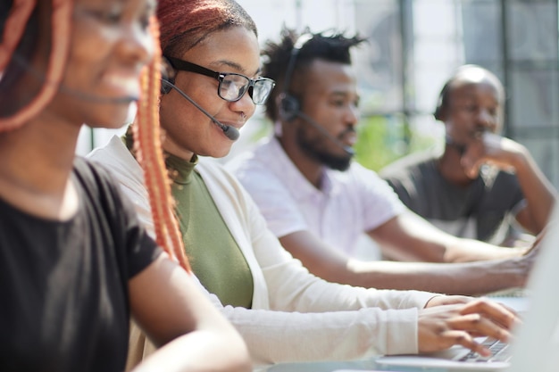 Foto sorrindo linda mulher afro-americana, trabalhando em call center com equipe diversificada