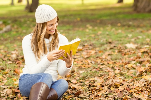 Sorrindo linda mulher lendo um livro em folhas