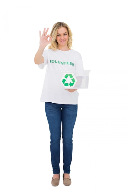 Sorrindo loira voluntário segurando a caixa de reciclagem, fazendo o gesto bem