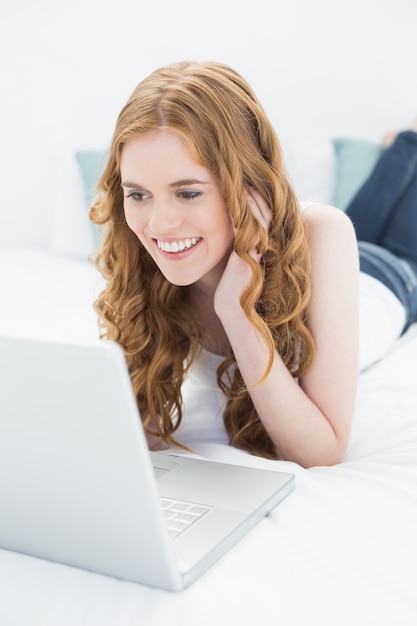 Sorrindo loiro casual usando o laptop na cama