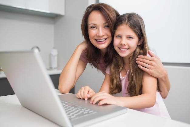 Sorrindo mãe com filha usando laptop na cozinha