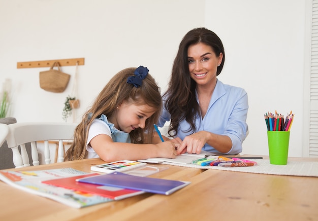 Sorrindo, mãe e filha se preparando para as aulas e desenha à mesa com lápis e tintas