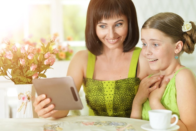 Sorrindo, mãe e filha sentada à mesa e usando tablet digital