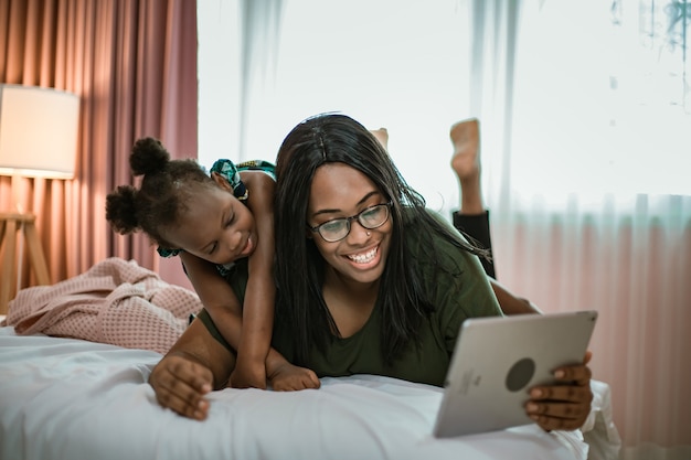 Sorrindo, mãe e filha usando o tablet do computador, fazendo videochamada juntos.