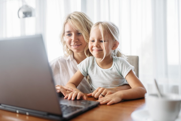 Sorrindo, mãe e filho usam o laptop em casa. Sentimento parental, união, família feliz