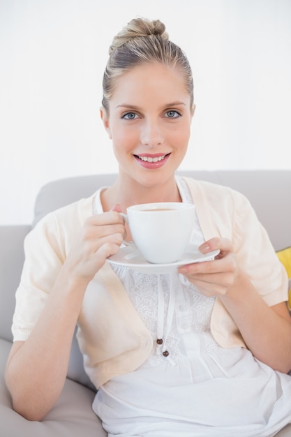 Sorrindo modelo fresco segurando café sentado no sofá