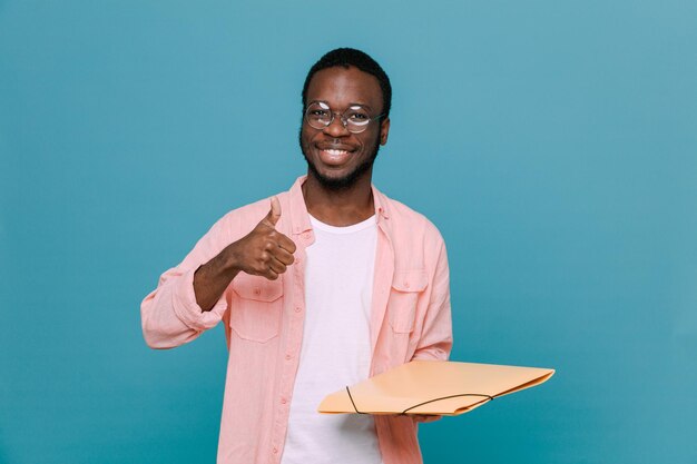 Sorrindo mostrando os polegares para cima segurando a pasta jovem afro-americano isolado em fundo azul