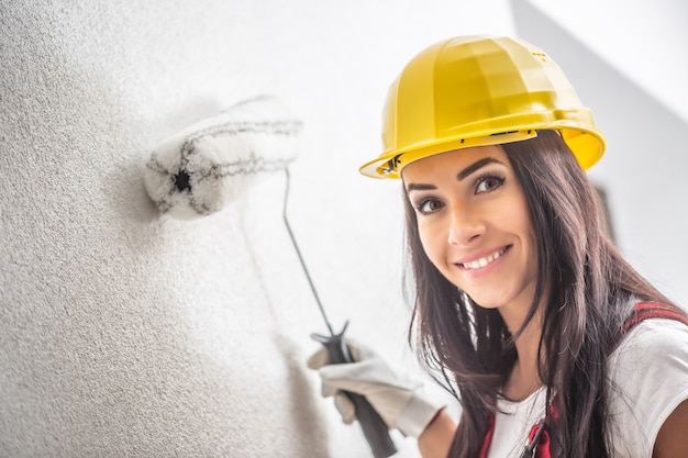 Sorrindo muito feminino com um capacete pintando a parede com um rolo.