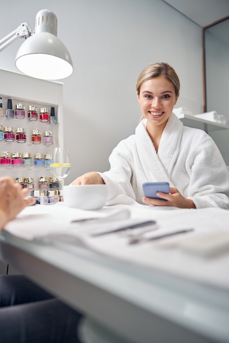 Foto sorrindo muito feminino com um copo d'água segurando a mão na banheira para os dedos e usando o smartphone
