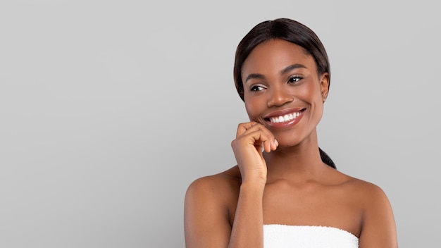 Sorrindo muito jovem afro-americana com cabelo brilhante na toalha, olhando para o espaço livre