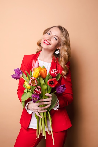 Sorrindo muito jovem com buquê de tulipas no dia da mulher isolado em fundo bege. Conceito de férias