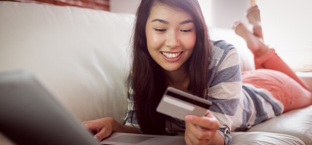 Sorrindo mulher asiática no sofá usando tablet para comprar on-line