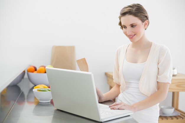 Sorrindo, mulher bonita, trabalhando com o caderno enquanto estava em sua cozinha