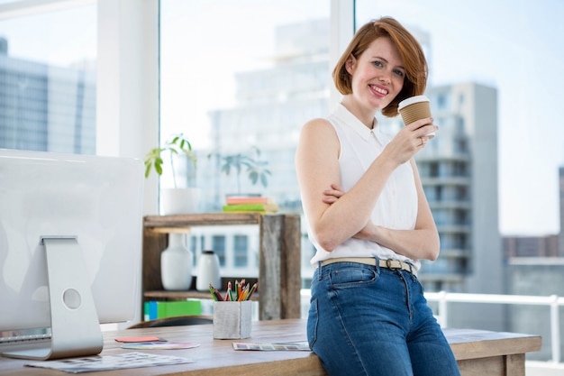 sorrindo mulher de negócios hipster, apoiando-se em sua mesa, bebendo café