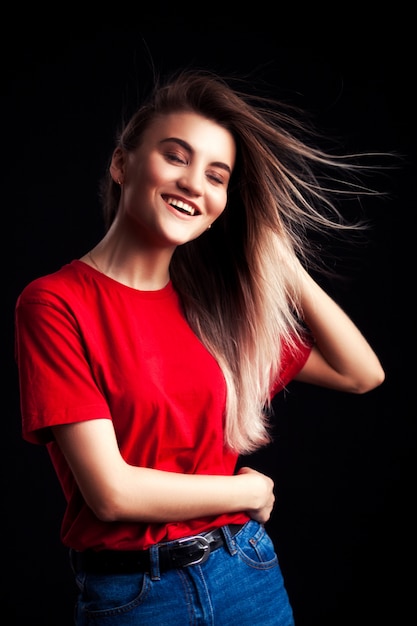 Sorrindo, mulher jovem bonita, em, vermelho, t-shirt, e, jaens, posar, com, mãos quadril