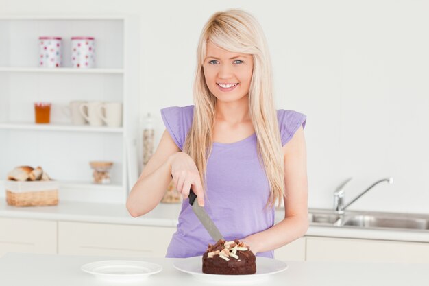 Sorrindo mulher loira cortando um bolo em um prato