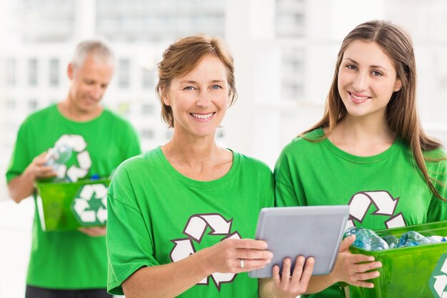 Sorrindo mulheres ecológicas com tablet e caixa de reciclagem